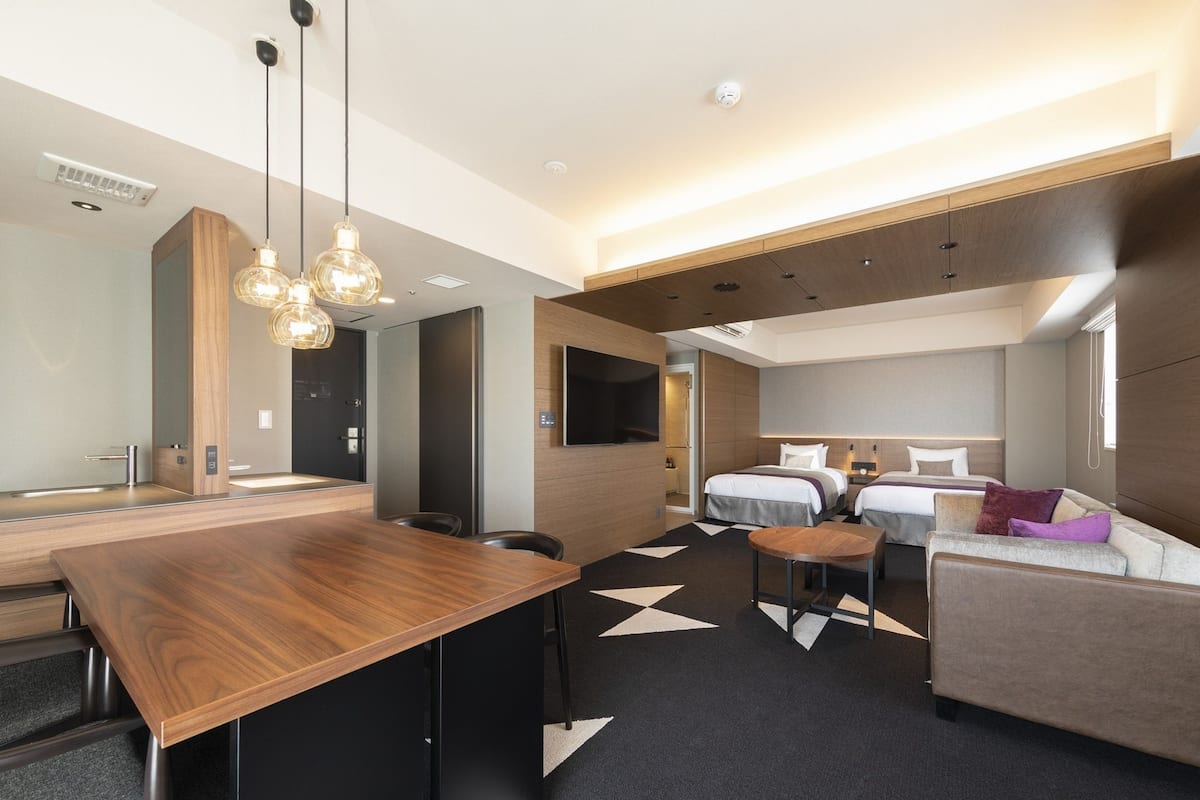 Une chambre d’hôtel moderne avec un bureau en bois, deux lits, un canapé et une télévision.