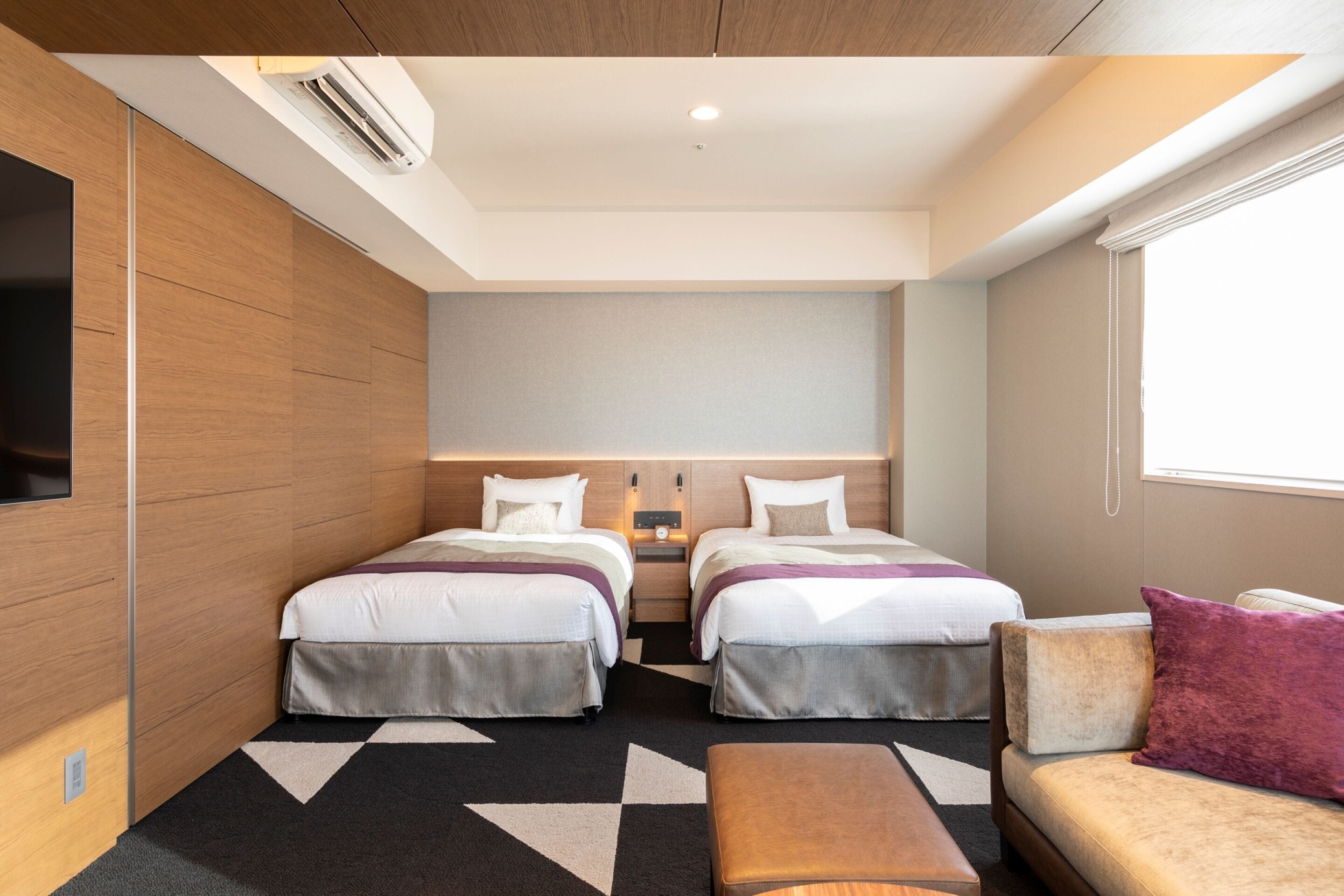 A hotel room with two beds, a sofa, a TV, and a window.
