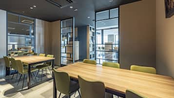 A modern conference room with a long table and chairs, large windows, and a visible kitchen area.
