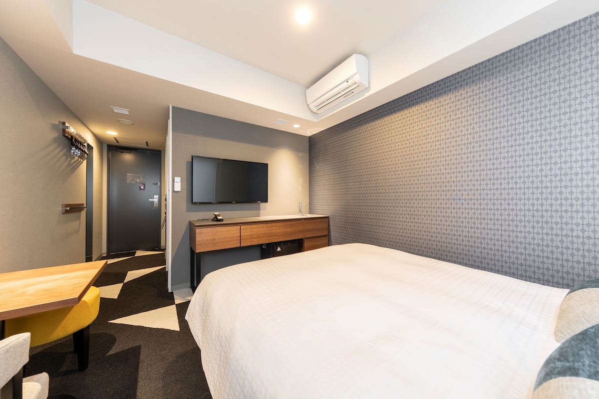 Une chambre d’hôtel équipée d’un lit, d’un bureau, d’une chaise, d’une télévision et d’un climatiseur fixé au mur.