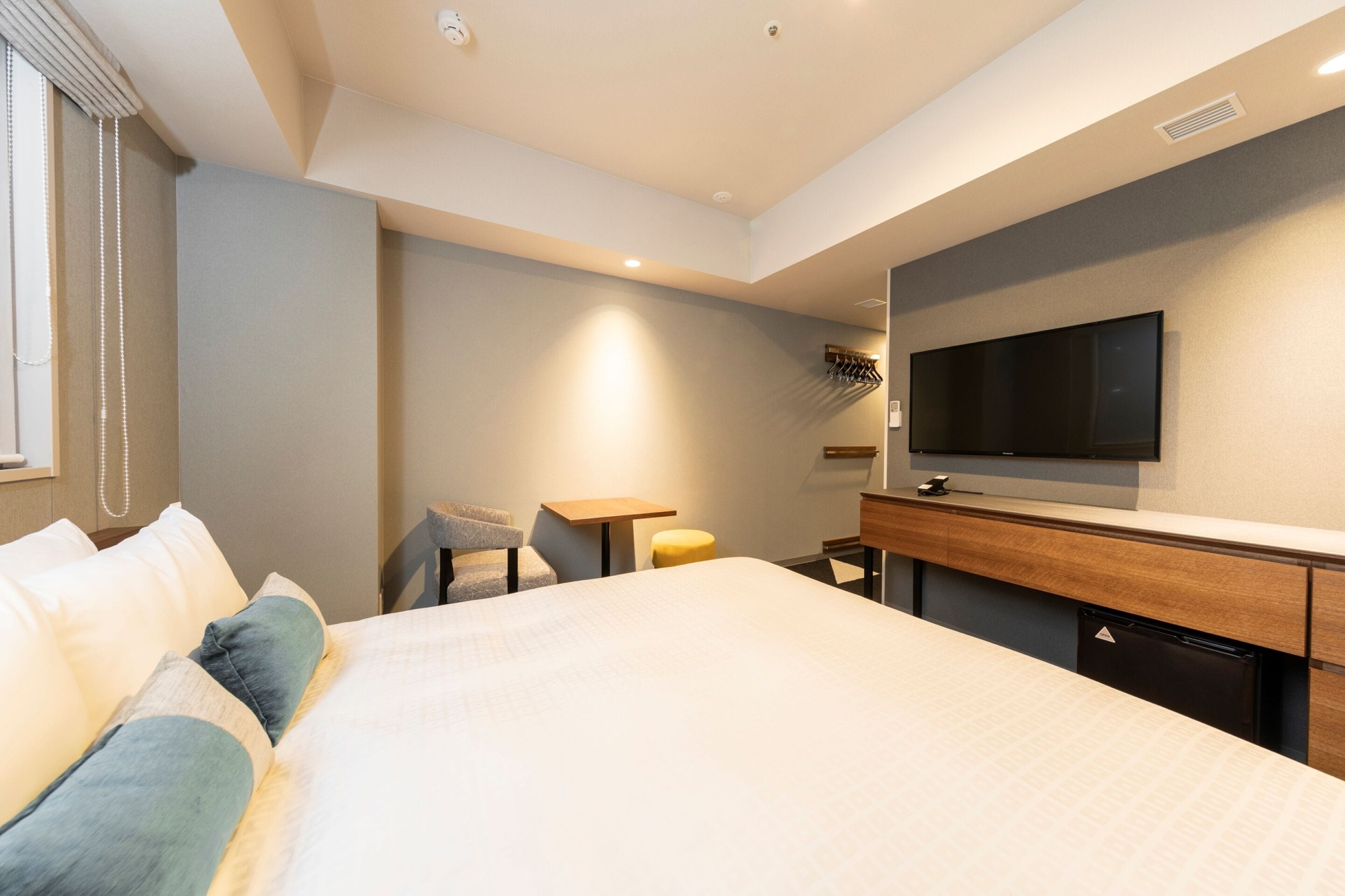 A modern hotel room with a large bed, a desk, a chair, a television, and a small table.