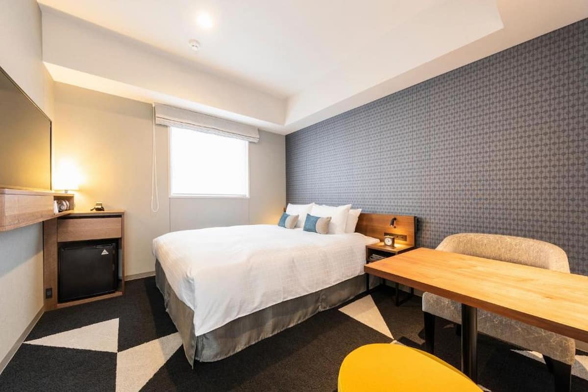 Une chambre d’hôtel comprenant un lit, une table de chevet, une lampe et un petit bureau avec une chaise.