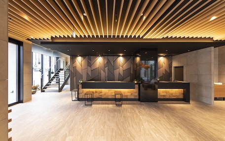 A modern reception area with a wooden ceiling, a reception desk, and a staircase leading to upper floors.