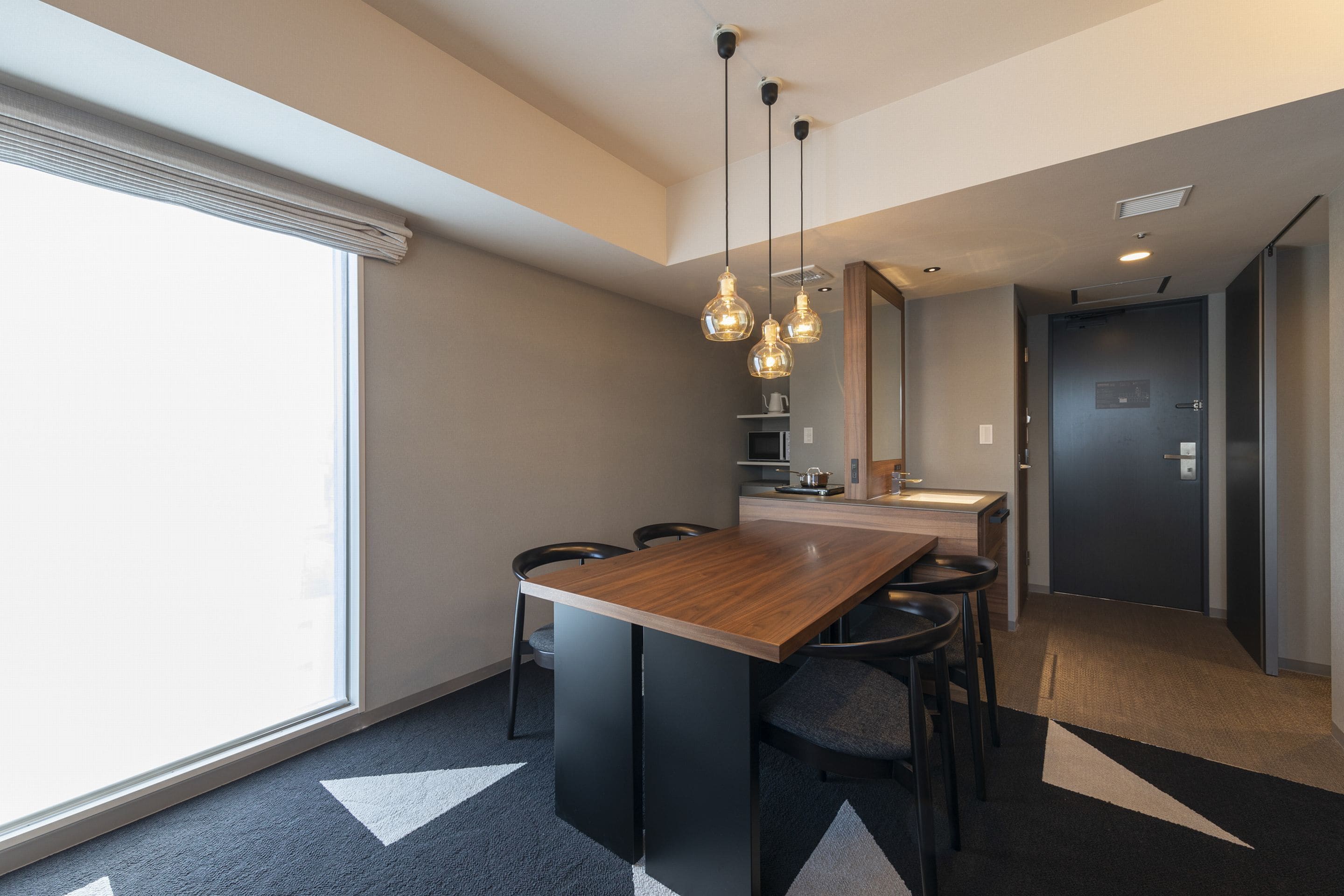 Une cuisine moderne avec un îlot central en bois, des chaises noires et des luminaires suspendus.