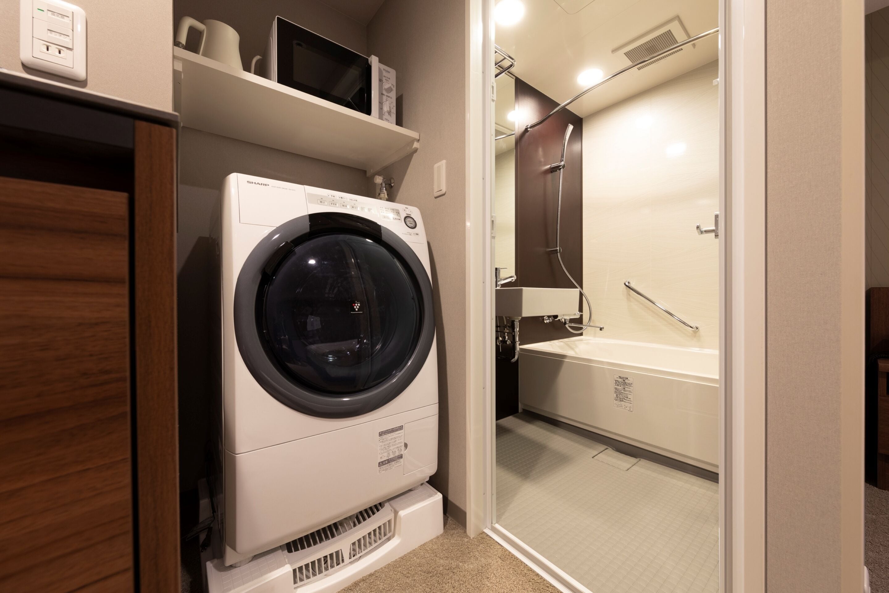 A compact laundry room with a front-loading washing machine, a shower area with a glass door, and a white sink.