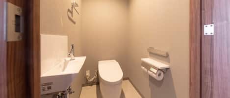 A small, modern bathroom with a white sink, toilet, and a toilet paper holder on the wall.
