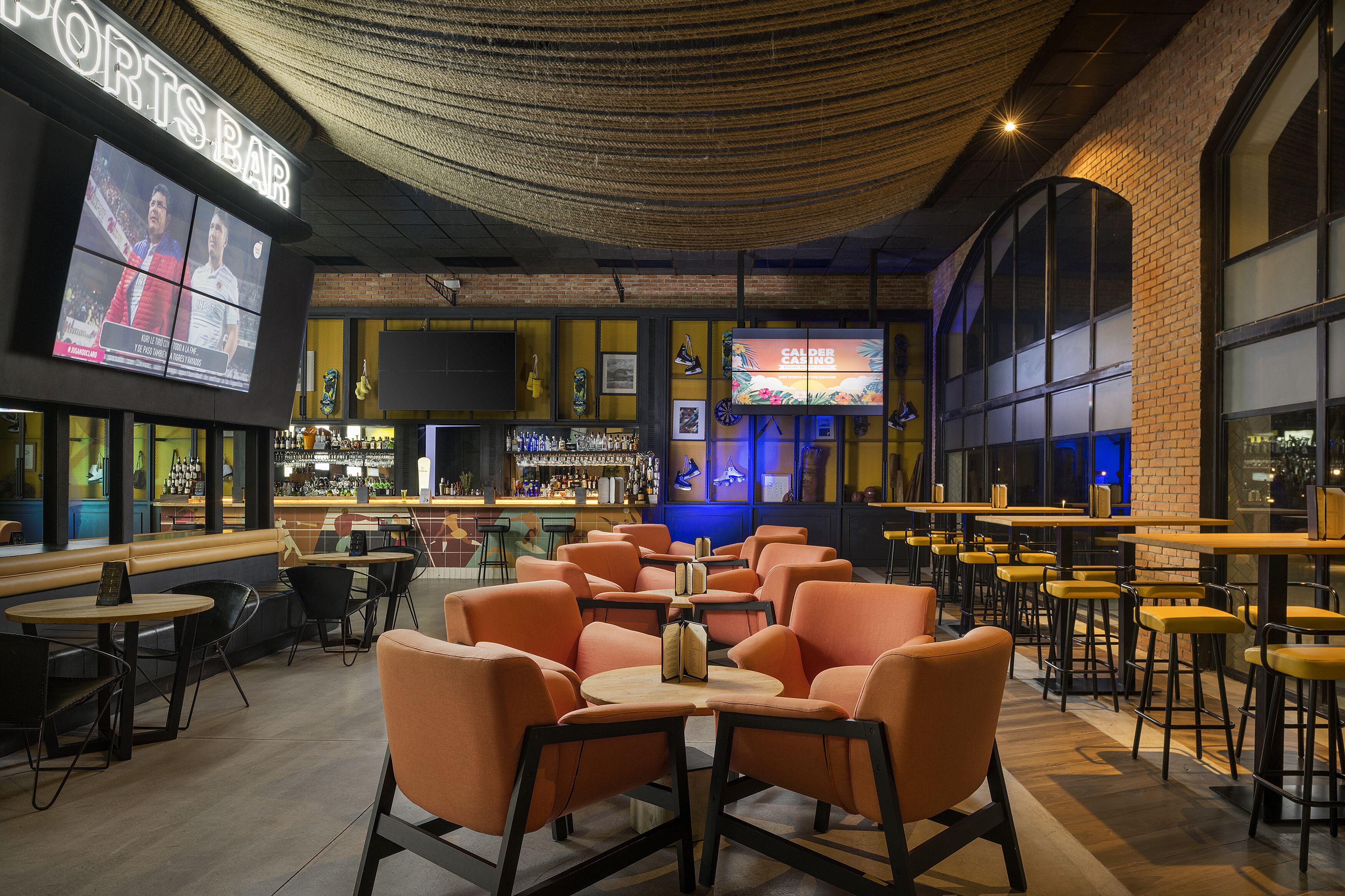 A sports bar with multiple seating areas, a bar counter, and a large screen displaying sports content.