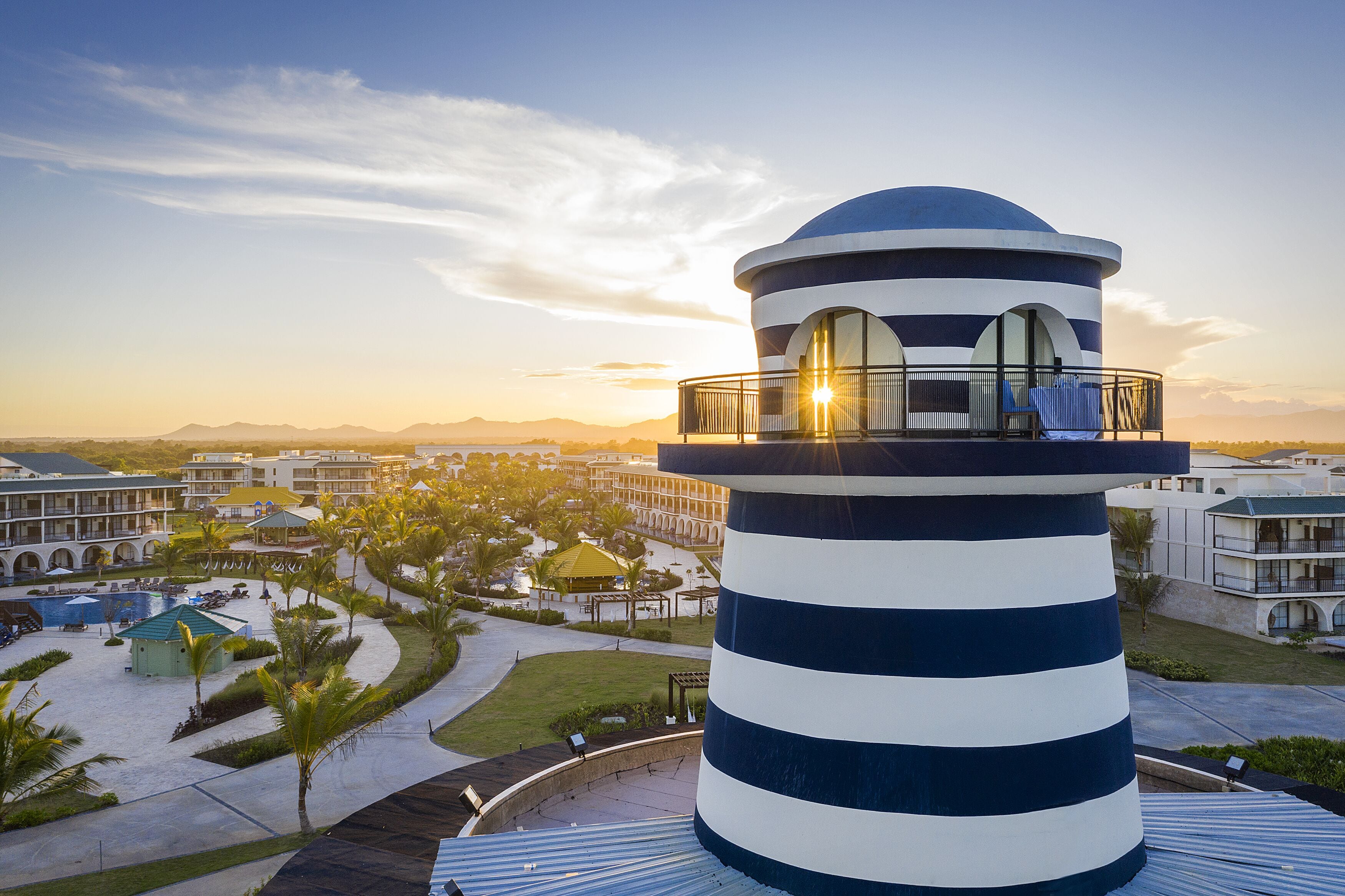Un edificio cilíndrico con balcón, rodeado por una zona de resort con piscinas y palmeras.