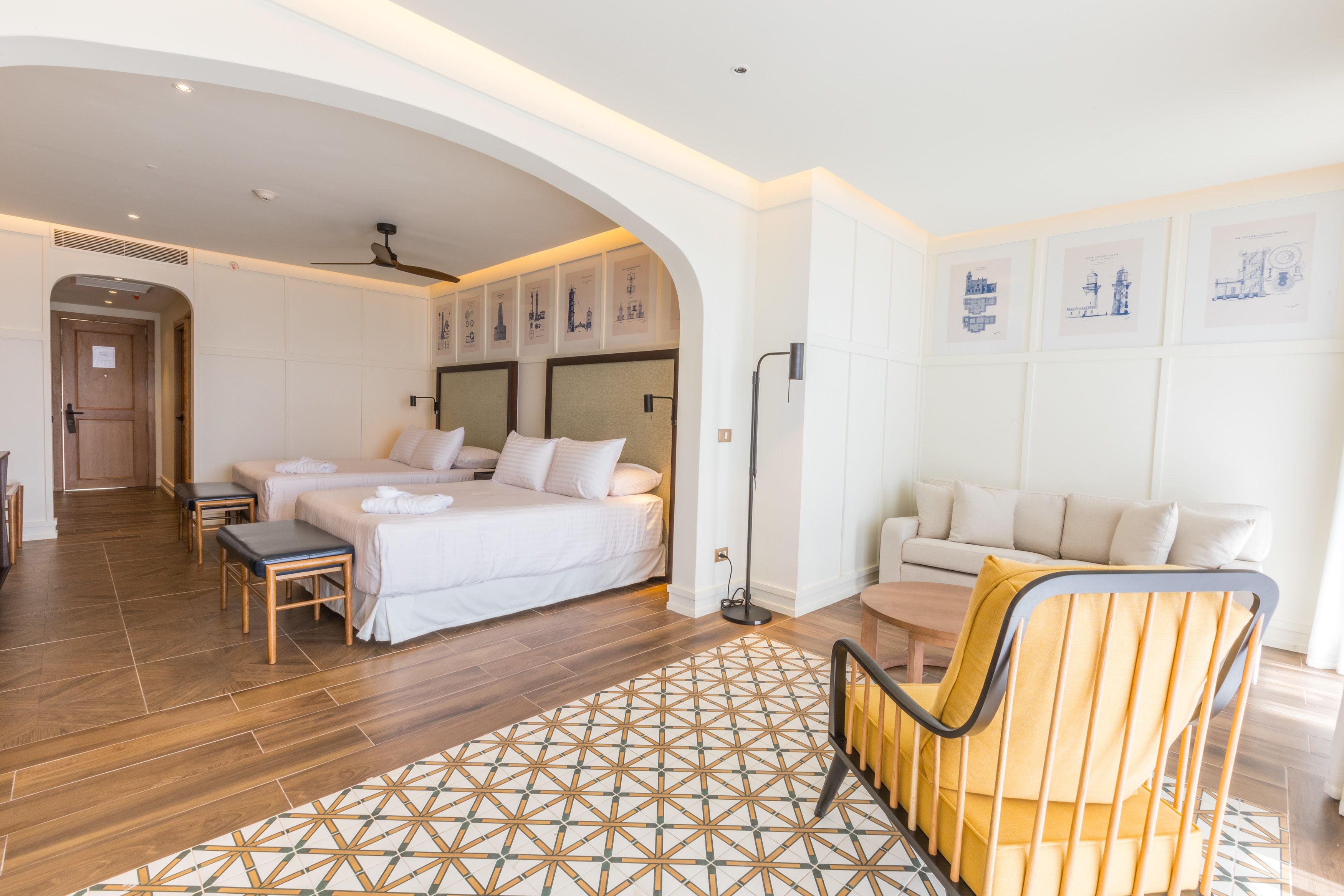 A hotel room with a large bed, a sofa, a chair, and a patterned rug.