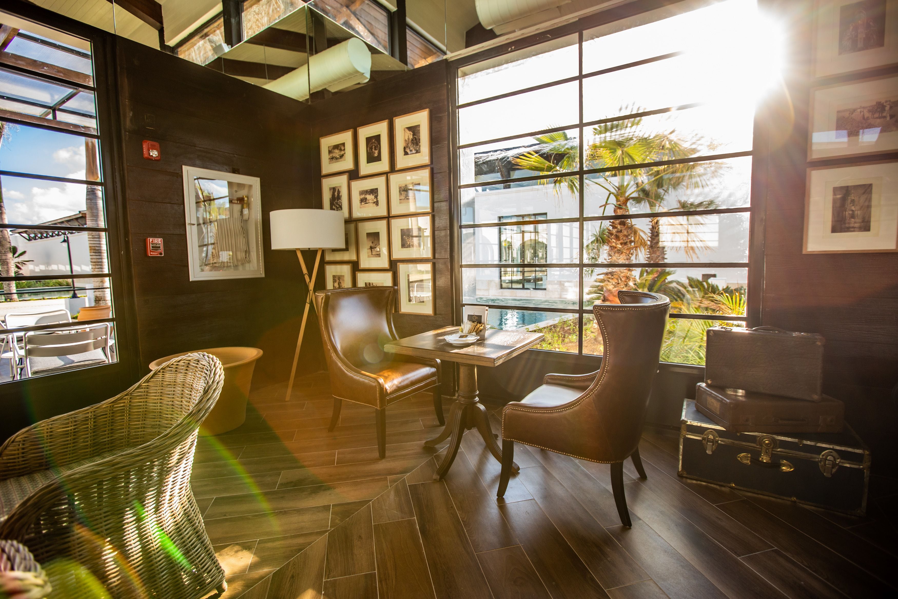 A room with a large window, wicker chairs, a table, and a wall decorated with framed pictures.