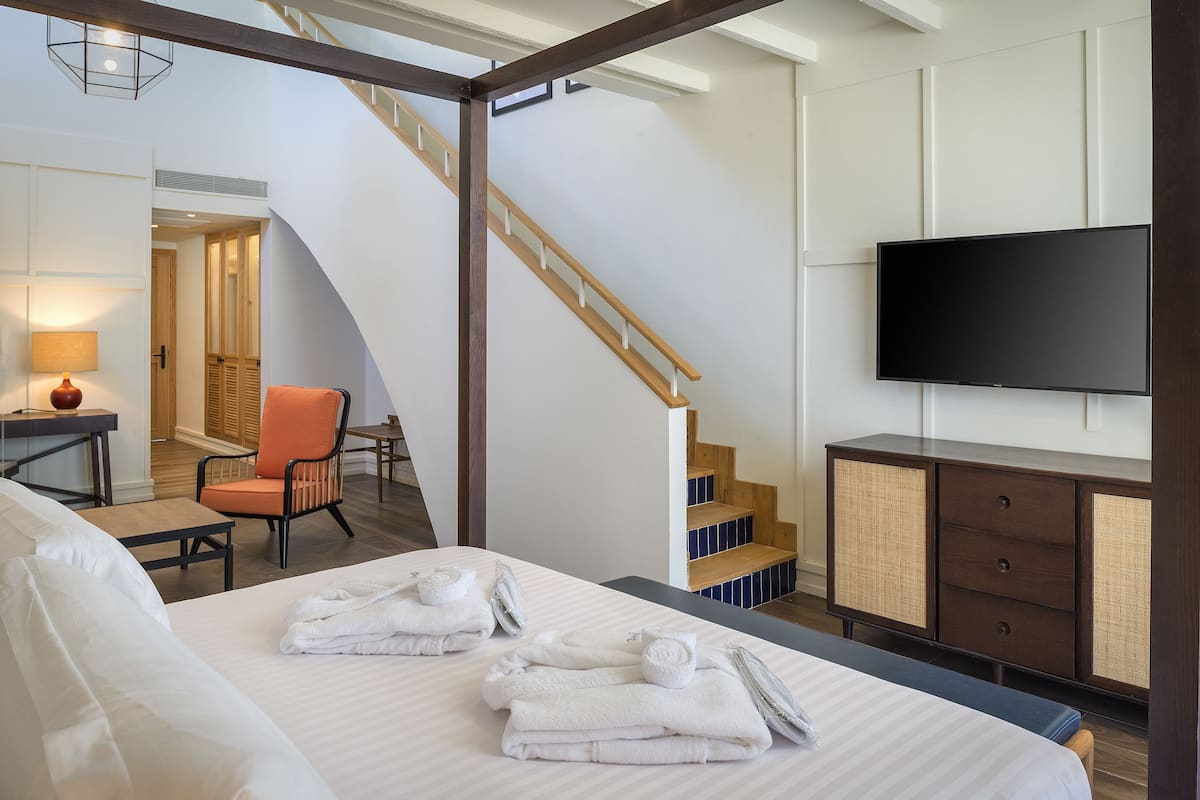 Une chambre d’hôtel avec un lit, une chaise, un bureau, une télévision et un escalier.