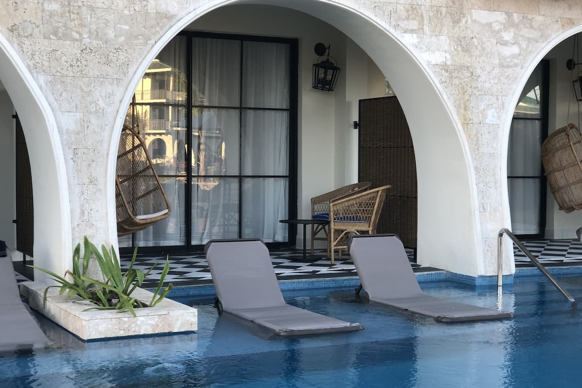Un espace piscine aménagé avec des chaises longues, un fauteuil en osier et une table sur laquelle se trouve un panier en osier.