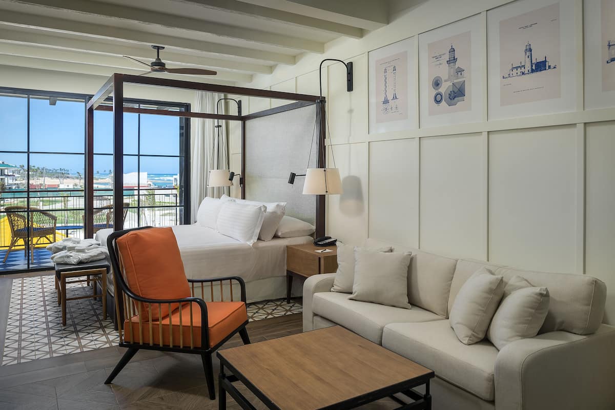Une chambre d’hôtel avec un lit à baldaquin, un canapé, une table en bois et une vue sur l’océan.