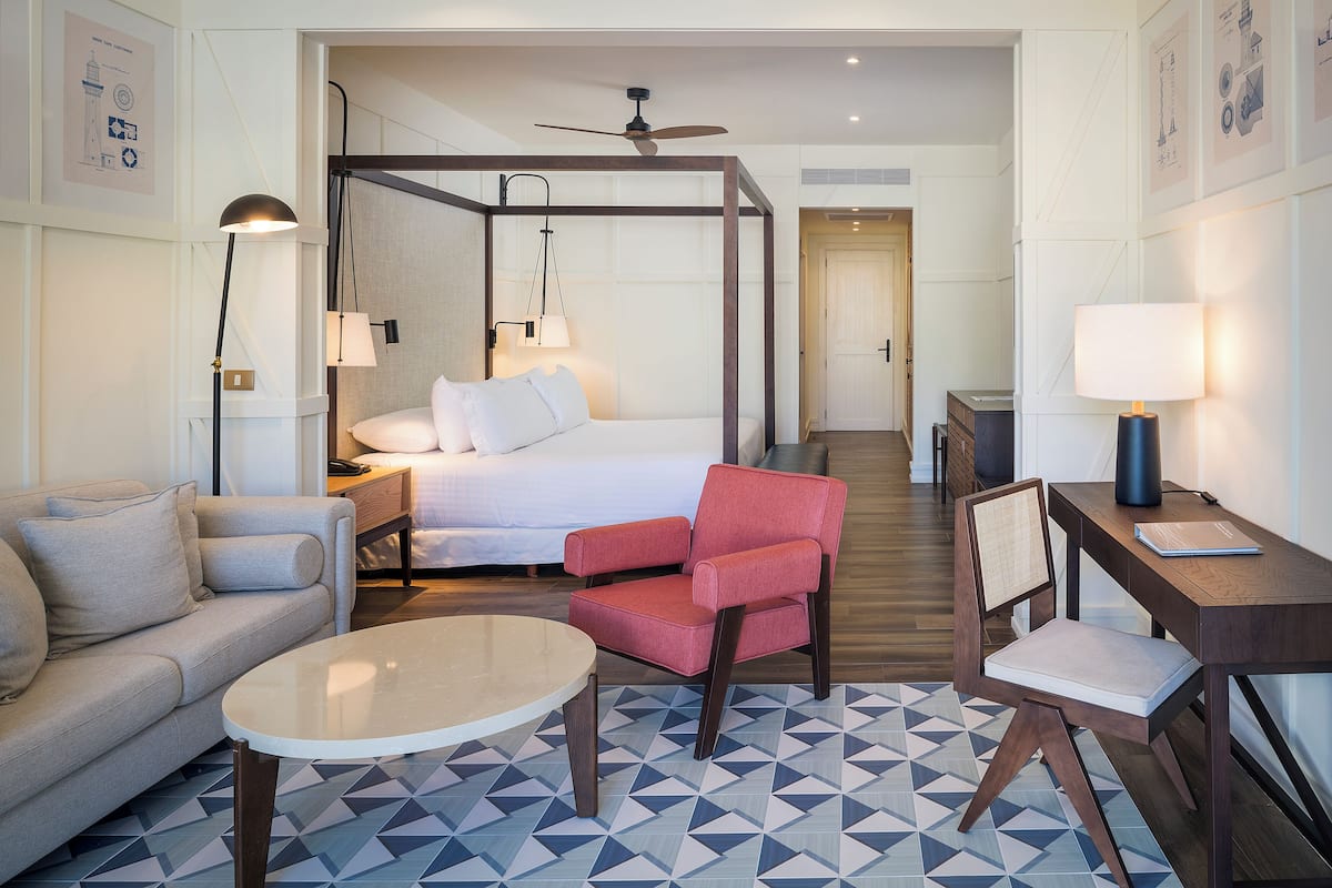 Une chambre d’hôtel avec un lit, un fauteuil rouge, un canapé, un bureau et une table basse.