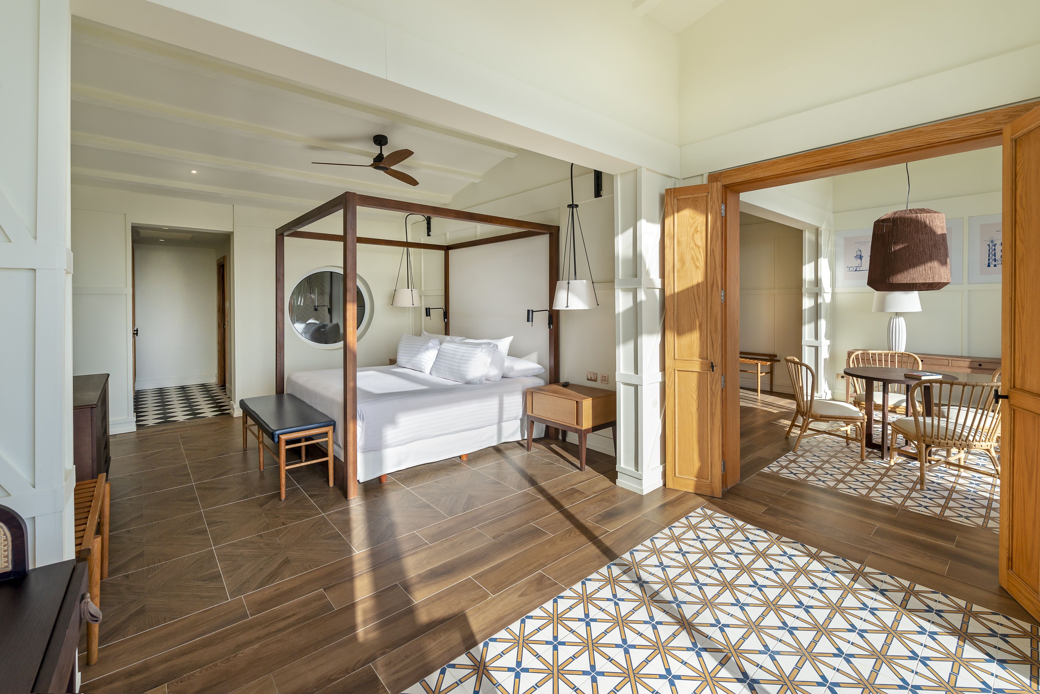 A bedroom with a four-poster bed, a desk, and a chair. There is a dining area with a table and chairs.