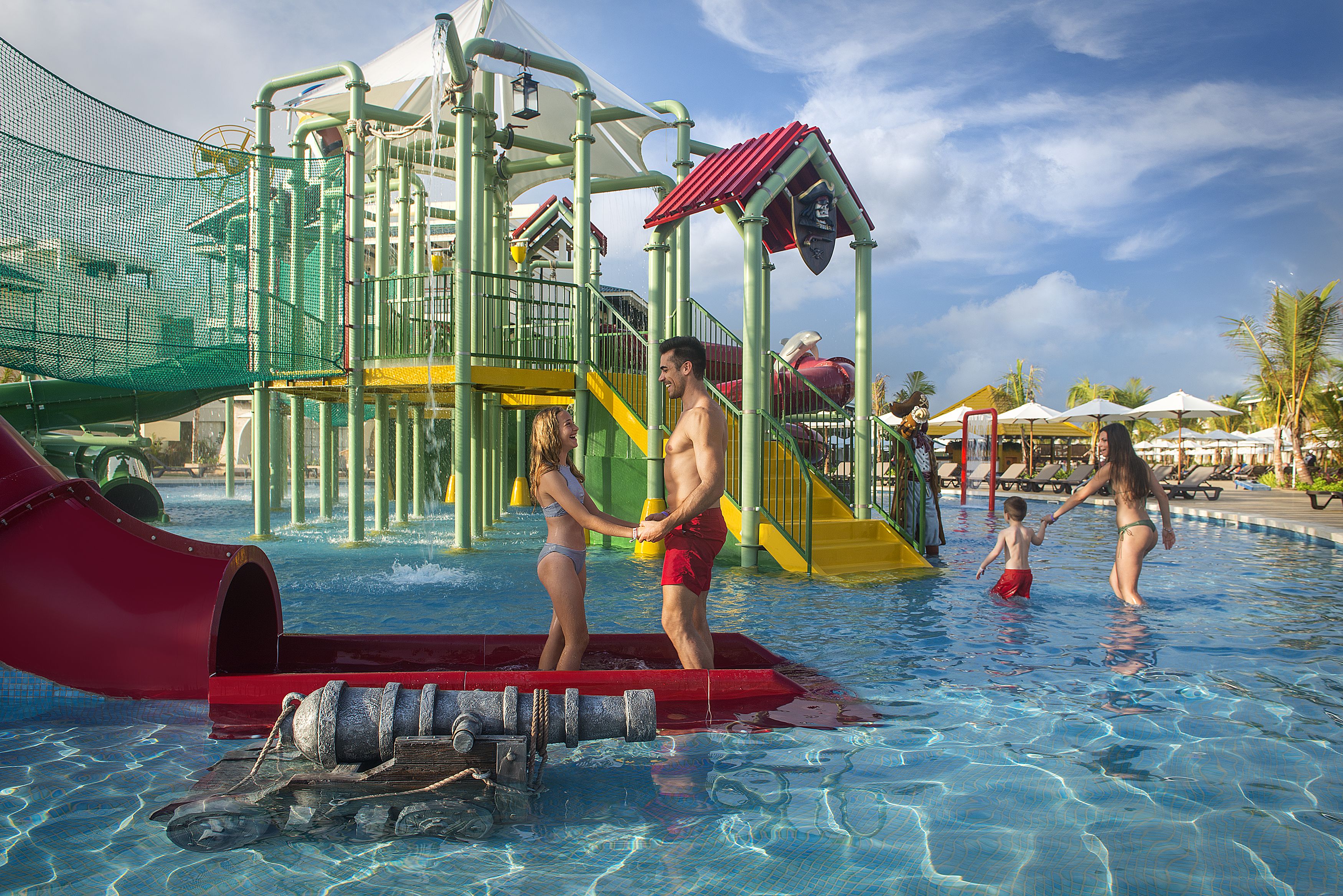 A water park with a red slide, a play structure, and a pool area.