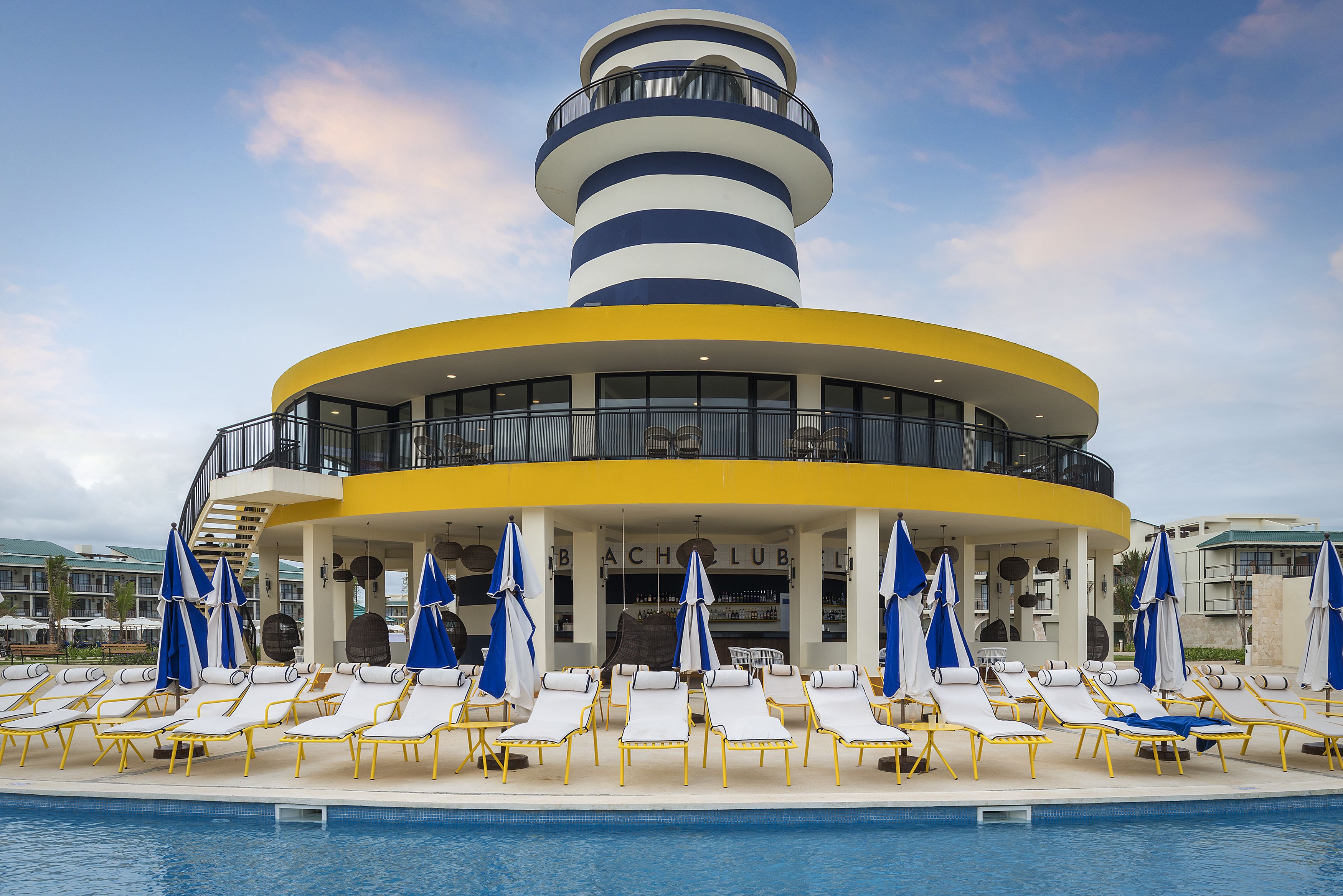 Un espace aménagé au bord de la piscine, avec des chaises longues et des parasols, un bar et une structure en forme de tour qui se distingue.