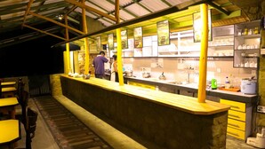 Un restaurante con una barra larga, sillas amarillas y una zona de cocina visible tras la barra.