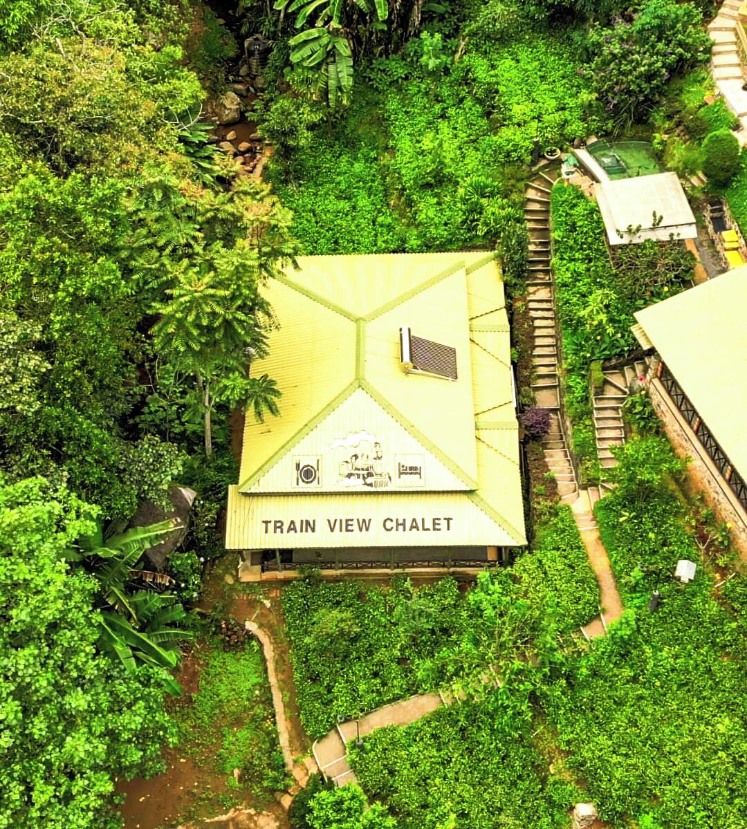 A 'TRAIN VIEW CHALET' with a hexagonal roof, surrounded by dense greenery and a small stream.