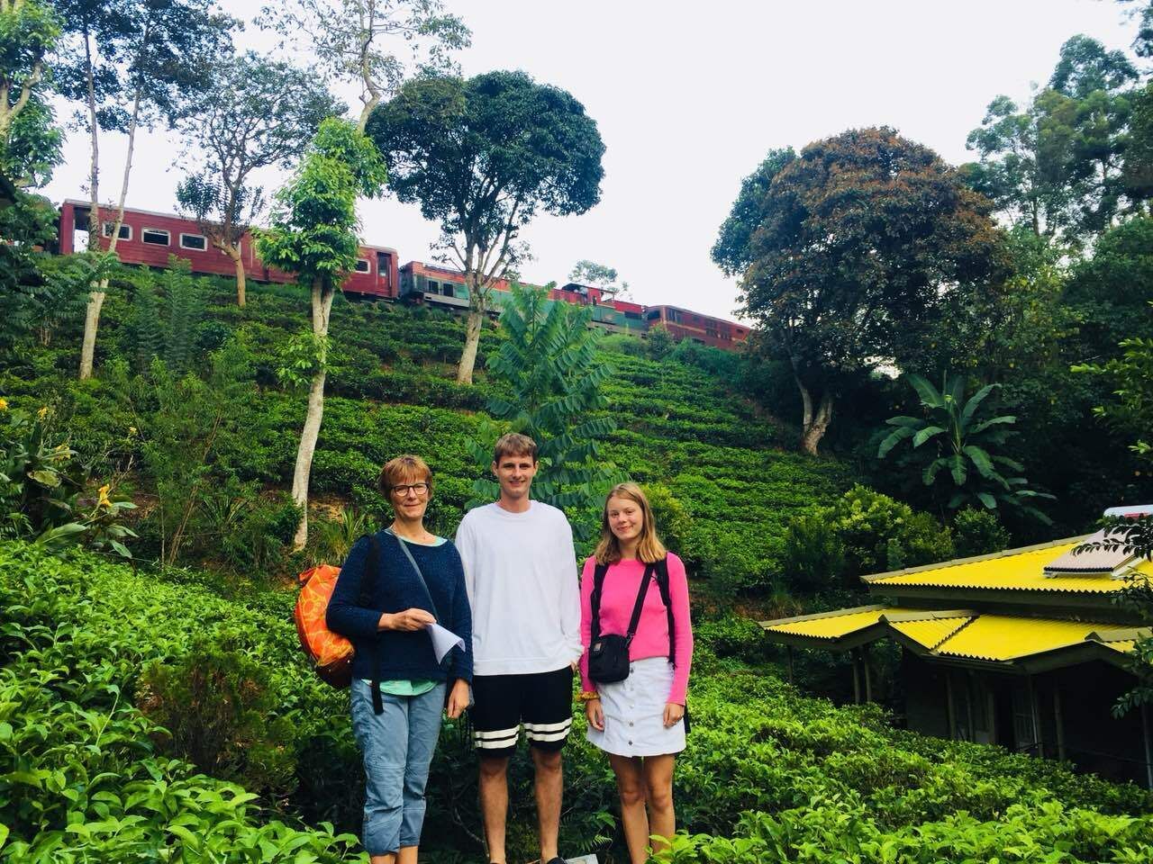 Tres personas de pie en una zona verde exuberante, con un edificio al fondo.