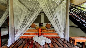 Una cama con dosel, escalones de madera y un banco con toallas.