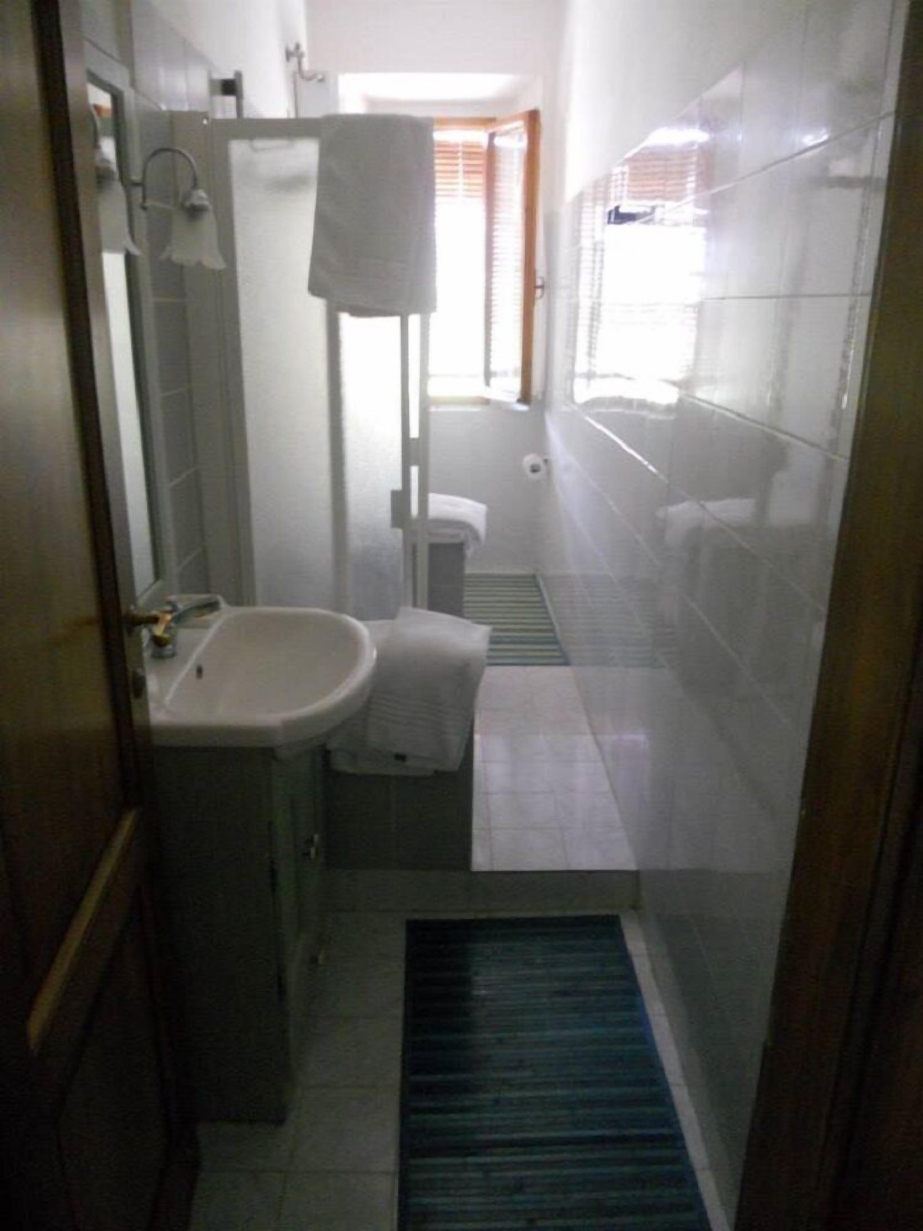Une petite salle de bain comprenant un lavabo, un miroir, un porte-serviettes et une petite fenêtre avec des stores.