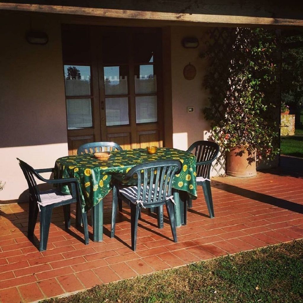 An outdoor patio with a table and chairs, a potted plant, and a building entrance.