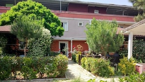 A residential building with a red facade, a covered porch, and a garden with various plants and a pathway leading to the entrance. - Deniz Kizi Otel (Armutlu)