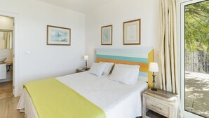 Un dormitorio con cama, mesita de noche, ventana con cortinas e imágenes enmarcadas en la pared.