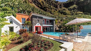Una casa moderna con piscina, rodeada de exuberante vegetación y montañas al fondo.