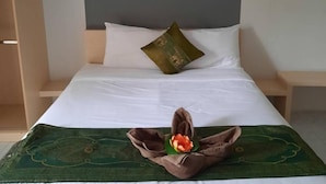 Una cama bien hecha con una colcha verde y blanca, una sola almohada marrón y un par de pantuflas marrones sobre la cama.