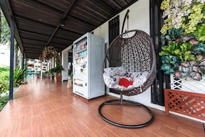 A covered outdoor area with a hanging chair, a vending machine, and a wall decorated with artificial flowers.