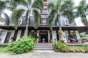 A modern building with a covered entrance, palm trees, and potted plants.