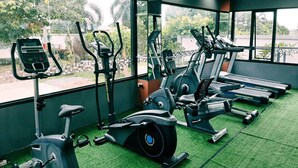 Un gimnasio con diferentes máquinas de ejercicio, amplias ventanas y vistas al exterior con zonas verdes.