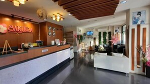 Zona de recepción de hotel con un mostrador de madera, un reloj y un televisor.