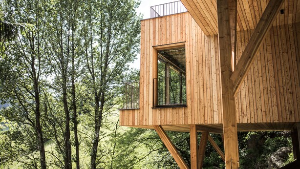 A wooden treehouse with a balcony, surrounded by tall trees. - Hotel Bad Fallenbach (San Leonardo in Passiria)