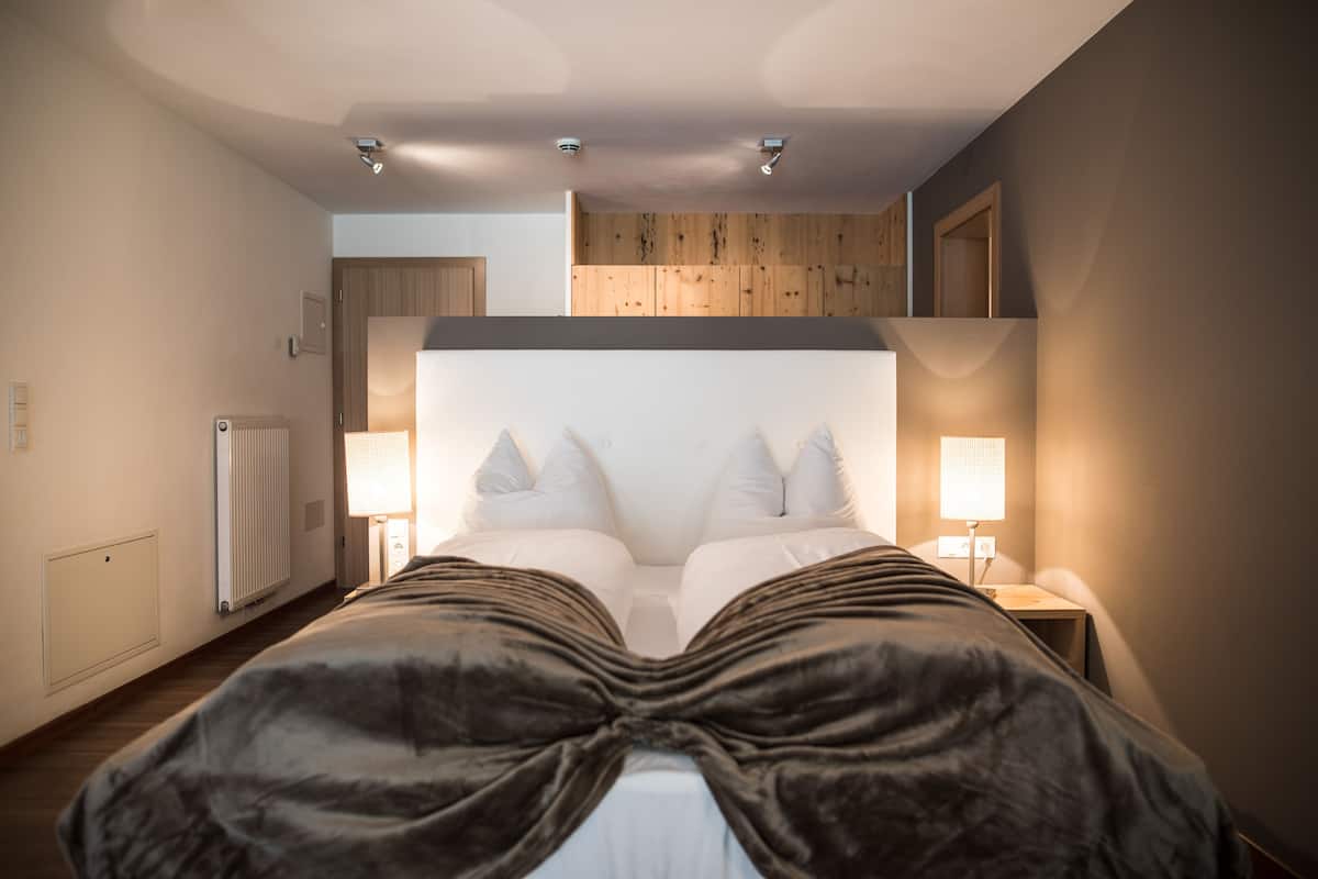 Un dormitorio con una cama grande, dos mesitas de noche con lámparas, techo de madera y un radiador en la pared.
