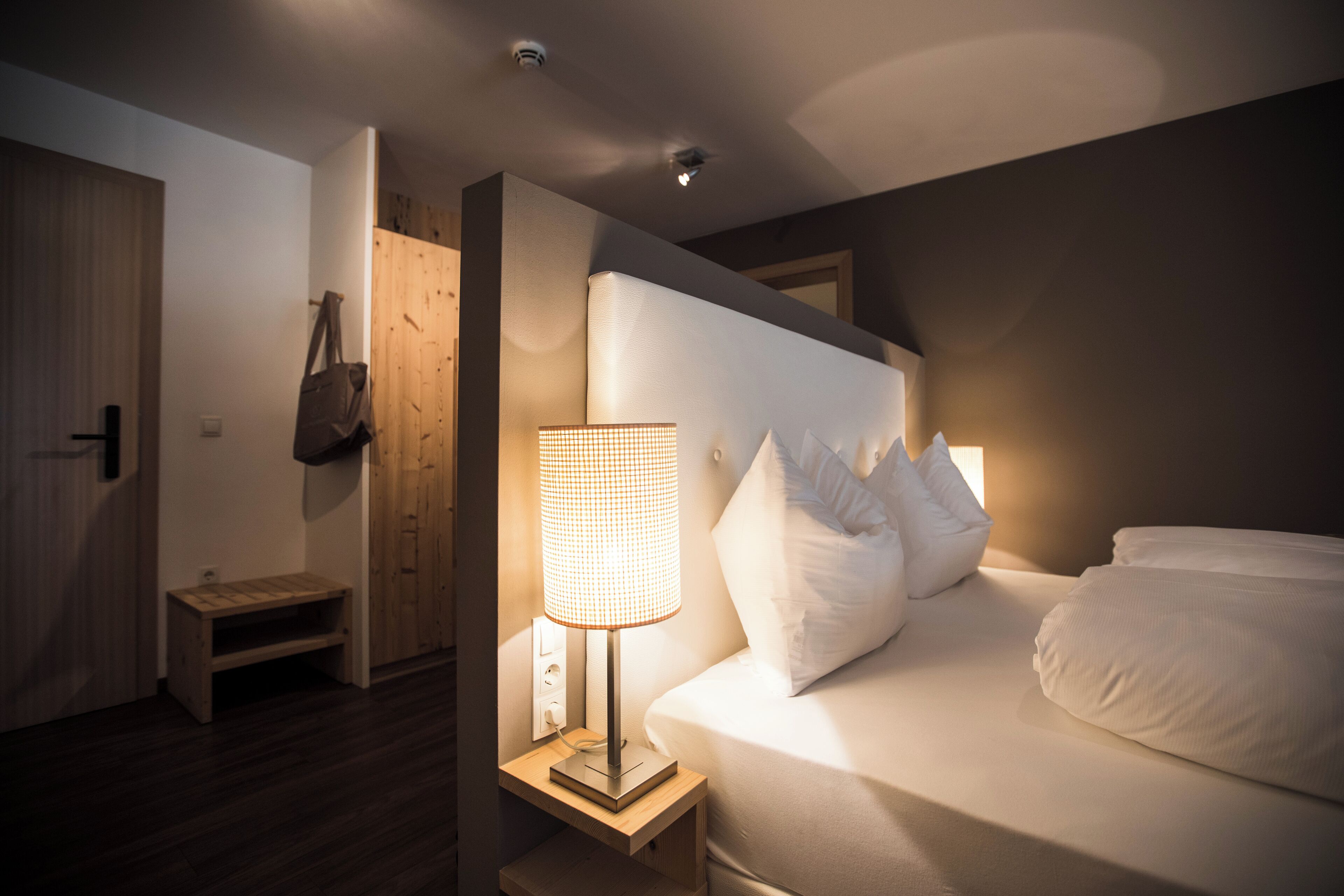 Un dormitorio con cama, lámpara de noche, banco de madera y una puerta.