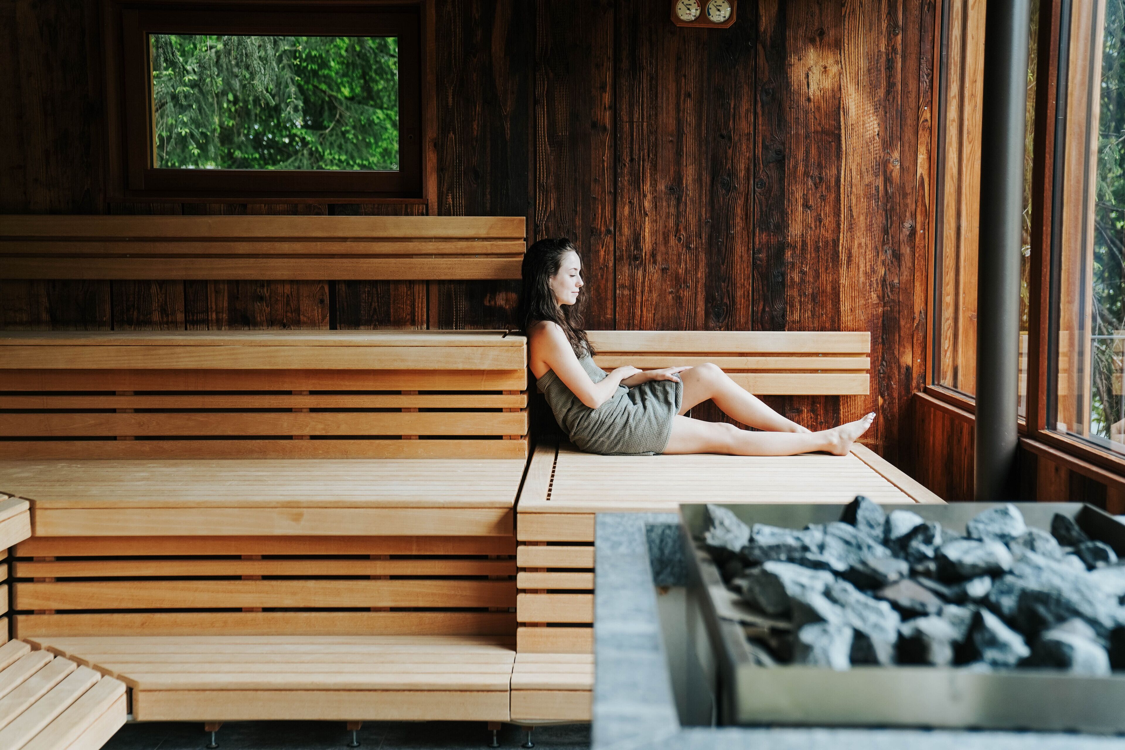 Un banco de madera con una persona sentada, una ventana que da a zonas verdes y una caja de carbón.
