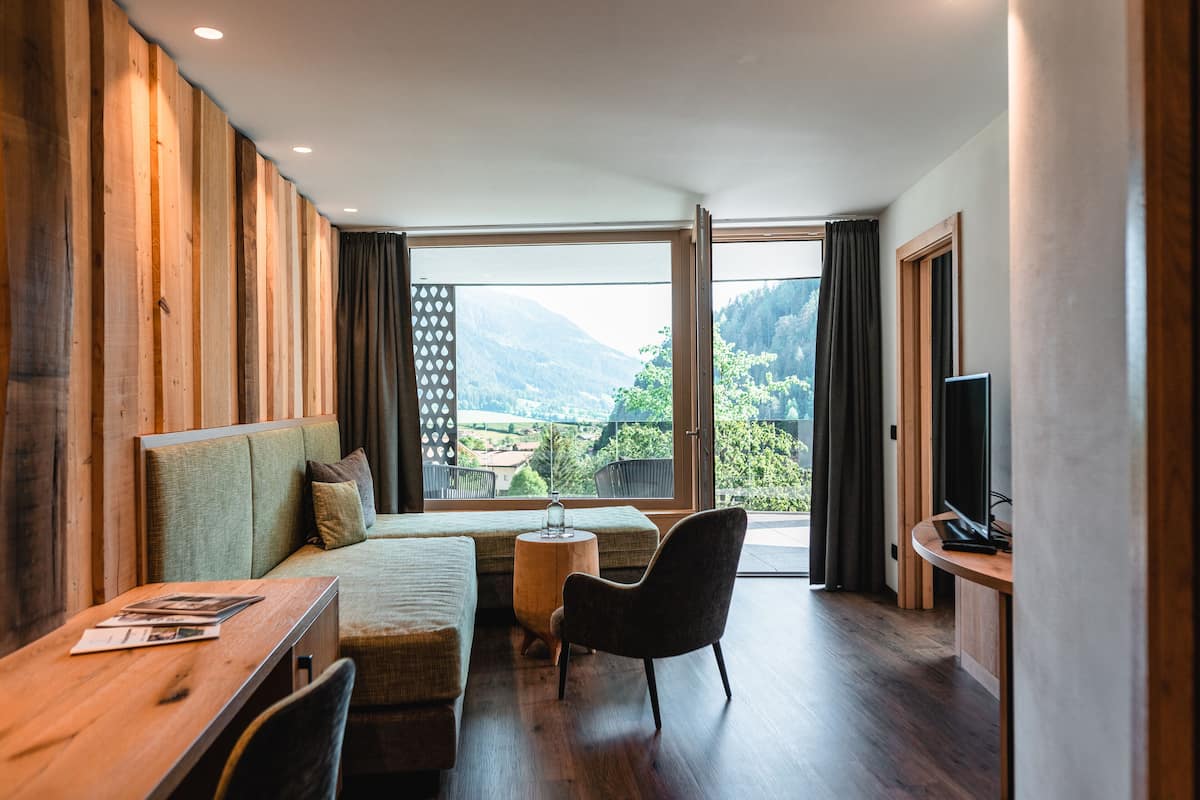 Una habitación moderna con sofá, una mesita, una silla, televisión y un amplio ventanal con vistas al exterior.