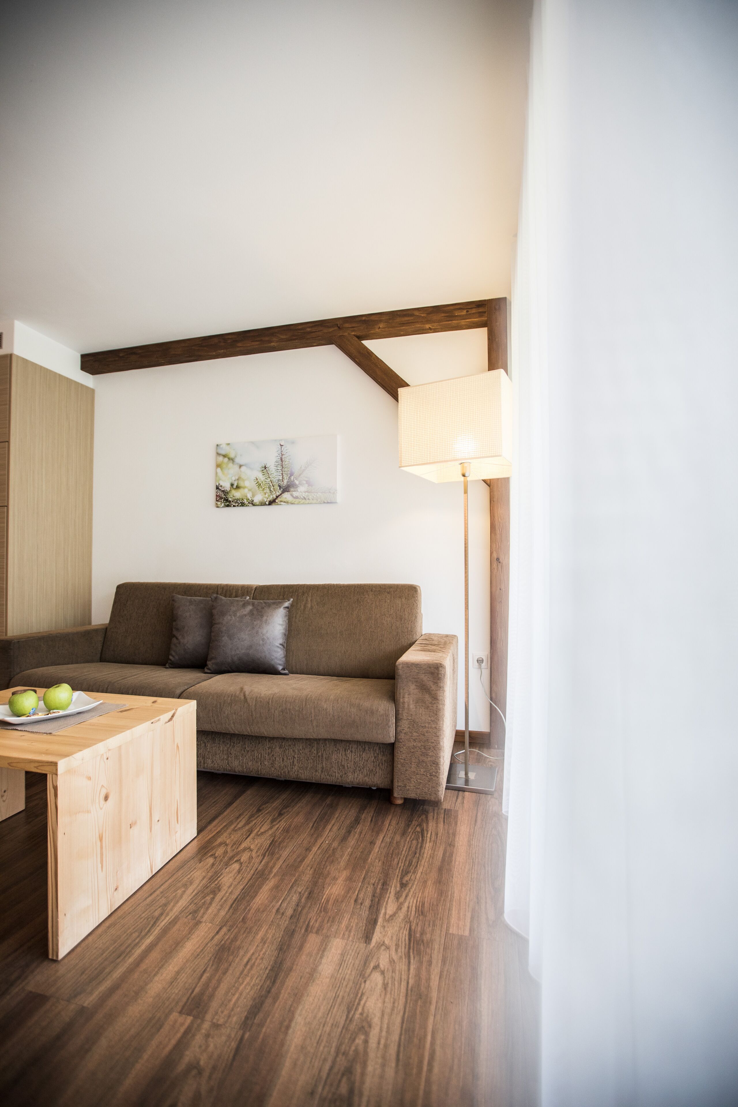 Un salon moderne avec un plancher en bois, un canapé marron, une table basse en bois et un lampadaire.