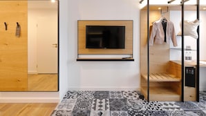 Una habitación moderna con un televisor montado en la pared, un armario de madera, un tapete estampado y un perchero con ropa.