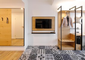 Una habitaci ón moderna con un televisor montado en la pared, un armario de madera, un tapete estampado y un perchero con ropa.
