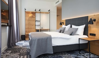 Una habitación de hotel moderna con una cama grande, lámparas de noche, un cabecero de madera y un suelo con diseño.