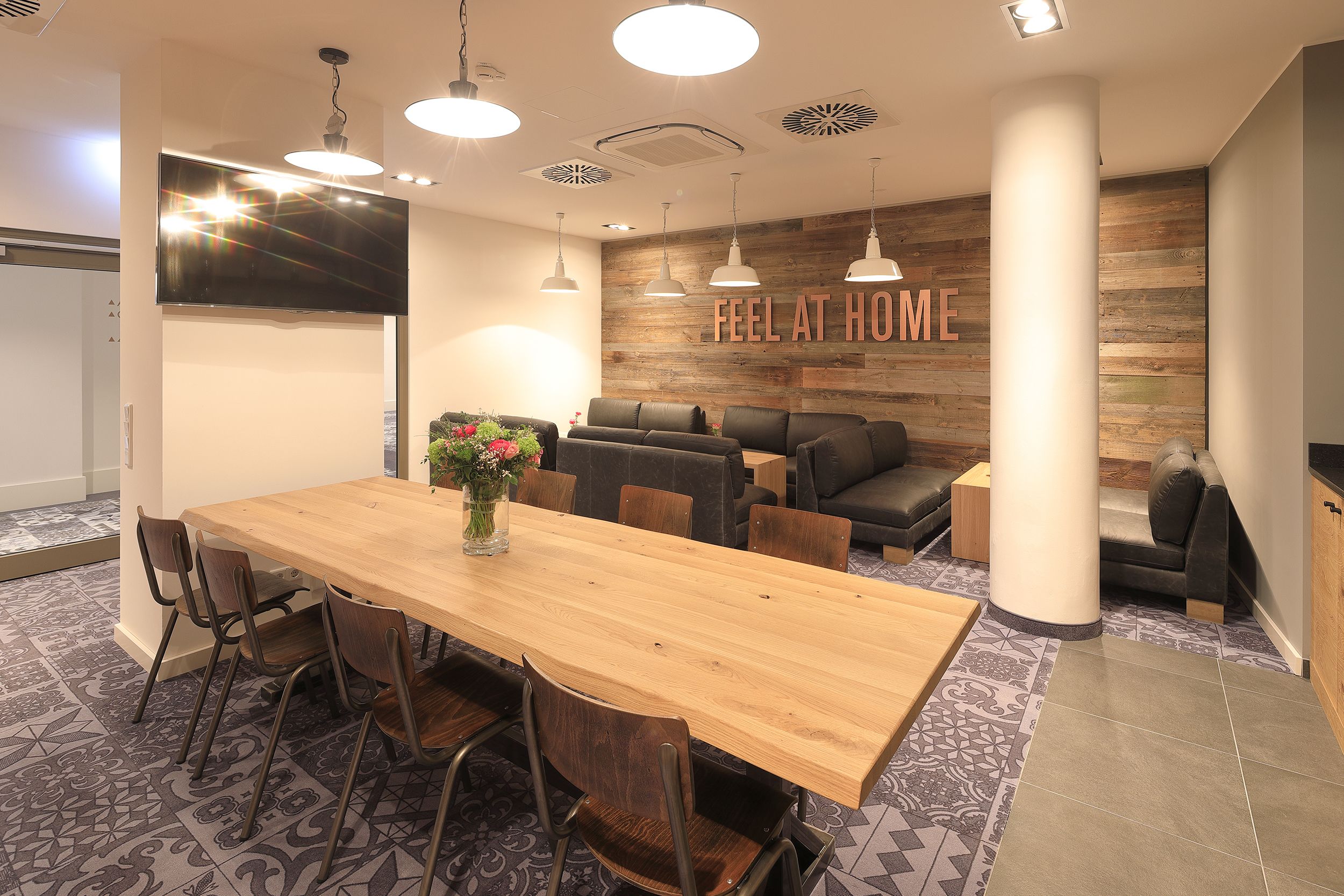 Una sala de reuniones moderna con una mesa de madera, sillas, un sofá y un televisor montado en la pared.