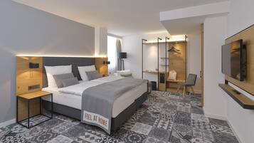 Una habitación de hotel moderna con una cama grande, mesitas de noche, un televisor, un armario y un suelo estampado.