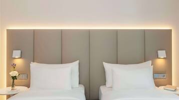 Una habitación de hotel con dos camas, una mesita de noche con lámpara, y una lámpara fijada a la pared.