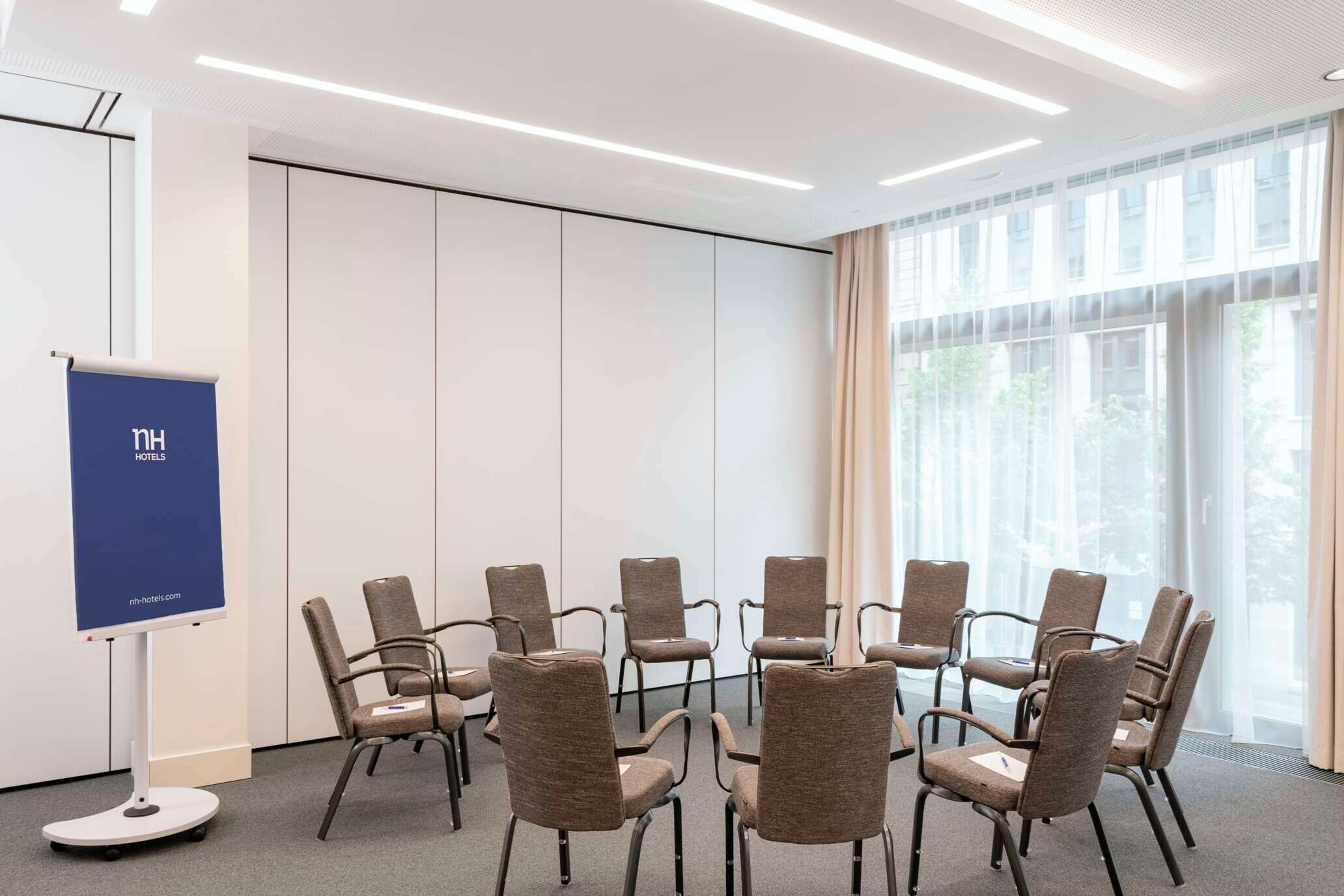 Una sala de conferencias con una mesa redonda y sillas, una pizarra y un ventanal con cortinas.
