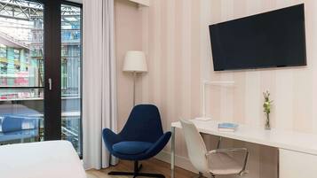 Ein Hotelzimmer mit Bett, Schreibtisch, Stuhl, Fernseher und einem Fenster mit Vorhängen.