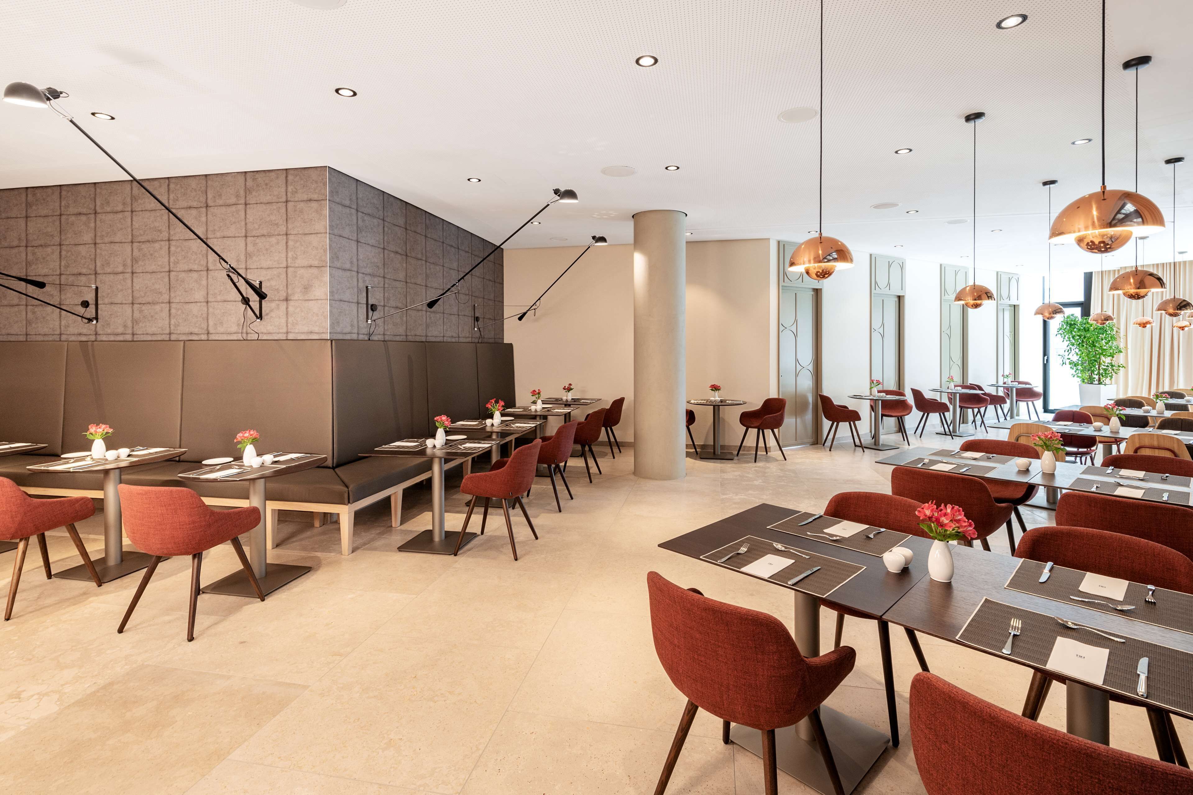 A modern restaurant with a long counter, multiple tables, and red chairs.
